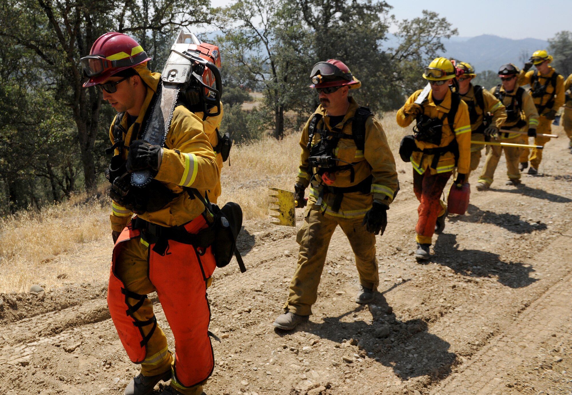 Steven Dobbs (left), 9th Civil Engineer Squadron fire captain, carries a chainsaw up a hill in front of other fire prevention organizations, Aug. 6, 2015, near Clearlake, California. The firefighters were sent to clear brush away from burned sections of land to prevent embers from igniting unburned areas. (U.S. Air Force Photo by Airman Preston L. Cherry)
