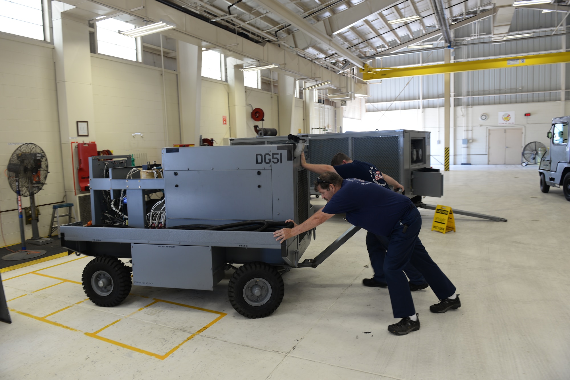 ALTUS AIR FORCE BASE, Okla. – Rich Desnoyer, 97th Maintenance Directorate Aerospace Ground Equipment Flight Chief, helps push a portable generator with Robert Tiscler in Building 278, Aug. 5, 2015. Without portable A/C units some buildings could not go more than one week with cool air and buildings like the control tower and the 97th Communications Squadron’s network servers could shut down from overheating. (U.S. Air Force photo by Airman 1st Class Kirby Turbak/Released)