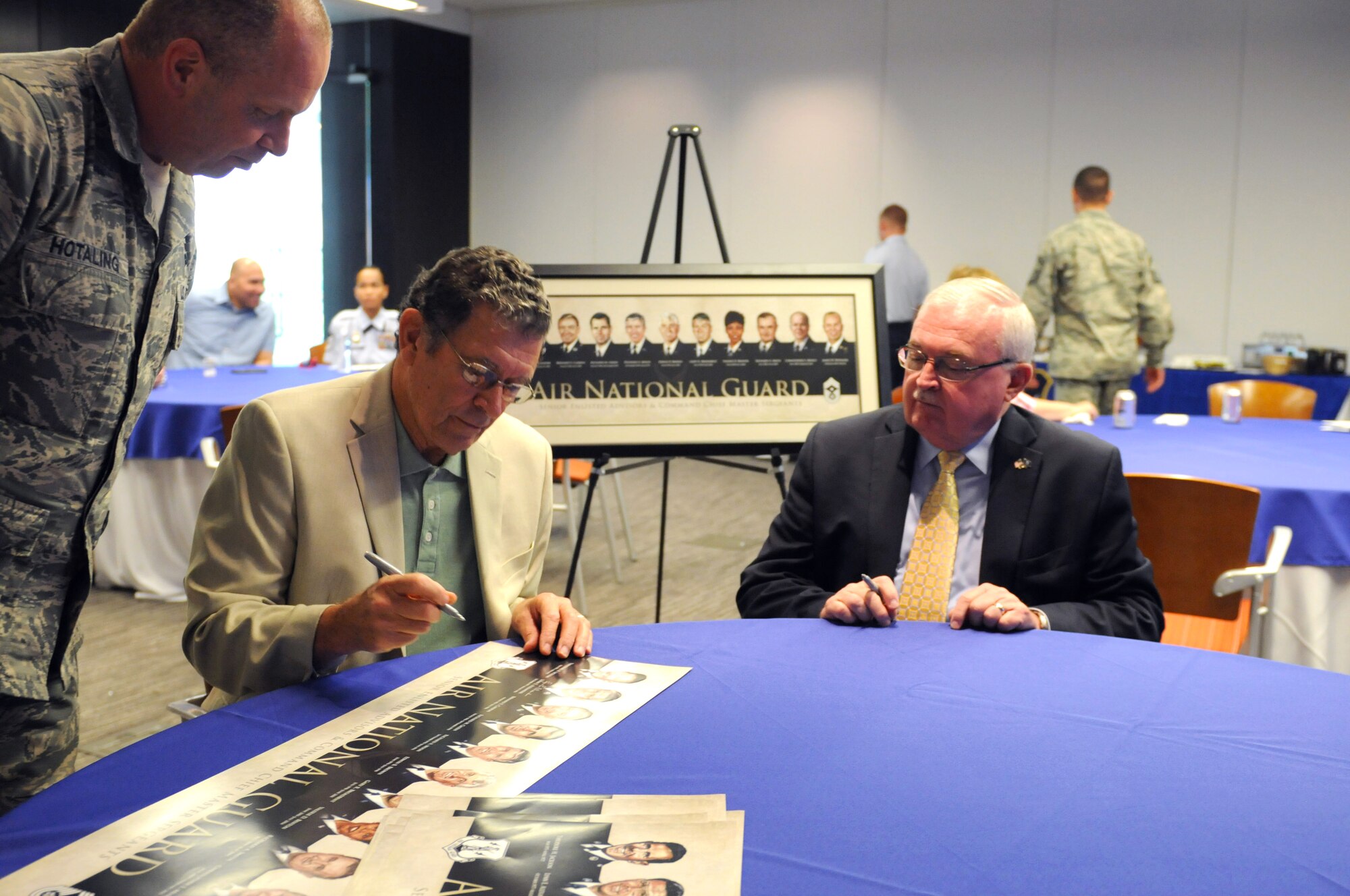 Retired Chief Master Sgt. Lynn E. Alexander, former Senior Enlisted Leader to the director of the Air National Guard, center, signs the formers heritage painting lithograph as Chief Master Sgt. James W. Hotaling, command chief master sergeant of the Air National Guard and retired Chief Master Sgt. Richard Smith, former command chief master sergeant of the Air National Guard observe. The lithograph was released as part of the ANG's Focus on the Force week, which gathers senior enlisted leadership to highlight the importance of professional development at all levels, receive feedback from junior enlisted Airmen, and tell the exceptional stories of ANG Airmen throughout the 50 states, territories, and the District of Columbia. (U.S. Air National Guard photo by Master Sgt. David Eichaker/released)