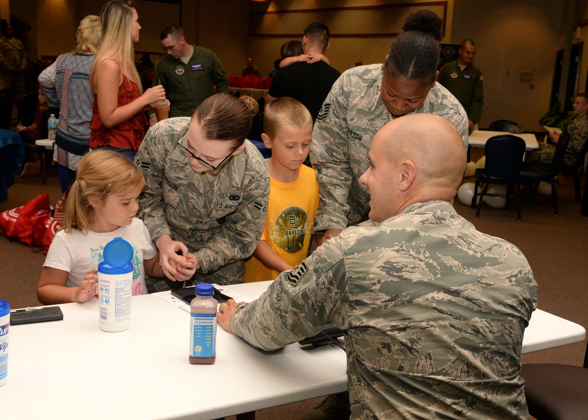 ALTUS AIR FORCE BASE, Okla. – U.S. Air Force Tech. Sgt. Joshua Leach, Tech. Sgt. Kristy Horton, and A1C Allie Harrison, 97th Security Forces Squadron members, fingeprint children during Operation Deploying Family at the Freedom Community Center, Aug. 5, 2015. Once finalized, the identification cards were provided to the children’s parents for safe keeping. (U.S. Air Force photo by Airman 1st Class Megan E. Acs/Released) 