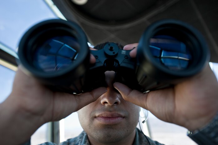 Airman 1st Class Cameron Cabrera, 57th Operations Support Squadron air traffic controller, looks at an aircraft on the runway through binoculars in the control tower on Nellis Air Force Base, Nev., Aug. 4, 2015. ATC Airmen manage the flow of air traffic on the ground and in 50,000 square miles of air space. (U.S. Air Force photo by Staff Sgt. Siuta B. Ika)