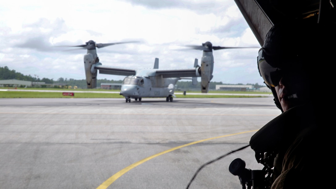 Corporal Kodi Floyd, a crew chief with Marine Medium Tiltrotor Squadron 365, Marine Air Group 26, communicates though a headset with the crew as two MV-22 Osprey aircrafts taxi on the flight line at Marine Corps Air Station New River, North Carolina, Aug. 4, 2015.  Marines with VMM-365 rehearsed different drop off and extraction scenarios at Landing Zone Bluebird and Landing Zone Bat at Camp Lejeune to maintain skills and standards within the squadron.