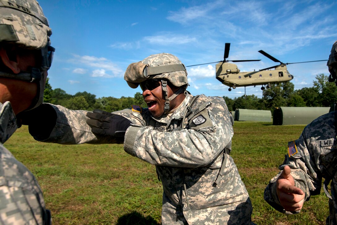 Army Reserve Sgt. Chantz Jackson, center, yells at his soldiers while a CH-47 Chinook helicopter lifts a boat bay during a slingload training operation at Fort Chaffee, Ark., July 31, 2015. Jackson is a bridge crew member assigned to the Army Reserves 341st Engineer Company, Multi-Role Bridge.