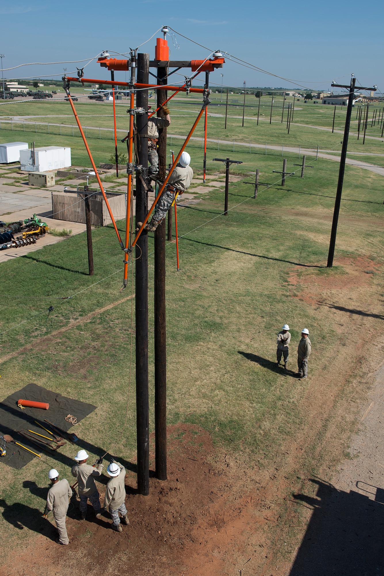 U.S. Air Force Staff Sgt. Andrew Goodrick, (left on the pole), from Nellis Air Force Base Nev., is a student in the 366th Training Squadron Hotline Training Course and native of Lawrence Kan., trains with Airman 1st Class Jaylen Wilkens, (right on the pole), from Charleston Air Force Base S.C., who is also a student in the course and native of Pittsburg Pa., at Sheppard Air Force Base, Texas, Aug. 7, 2015. Goodrick and Wilkens used special tools designed to remove safety wire that secures the power lines to the insulators. Airmen in this course wear a modified uniform to protect themselves from the various equipment and chemicals they use. (U.S. Air Force photo by Senior Airman Kyle Gese/Released)