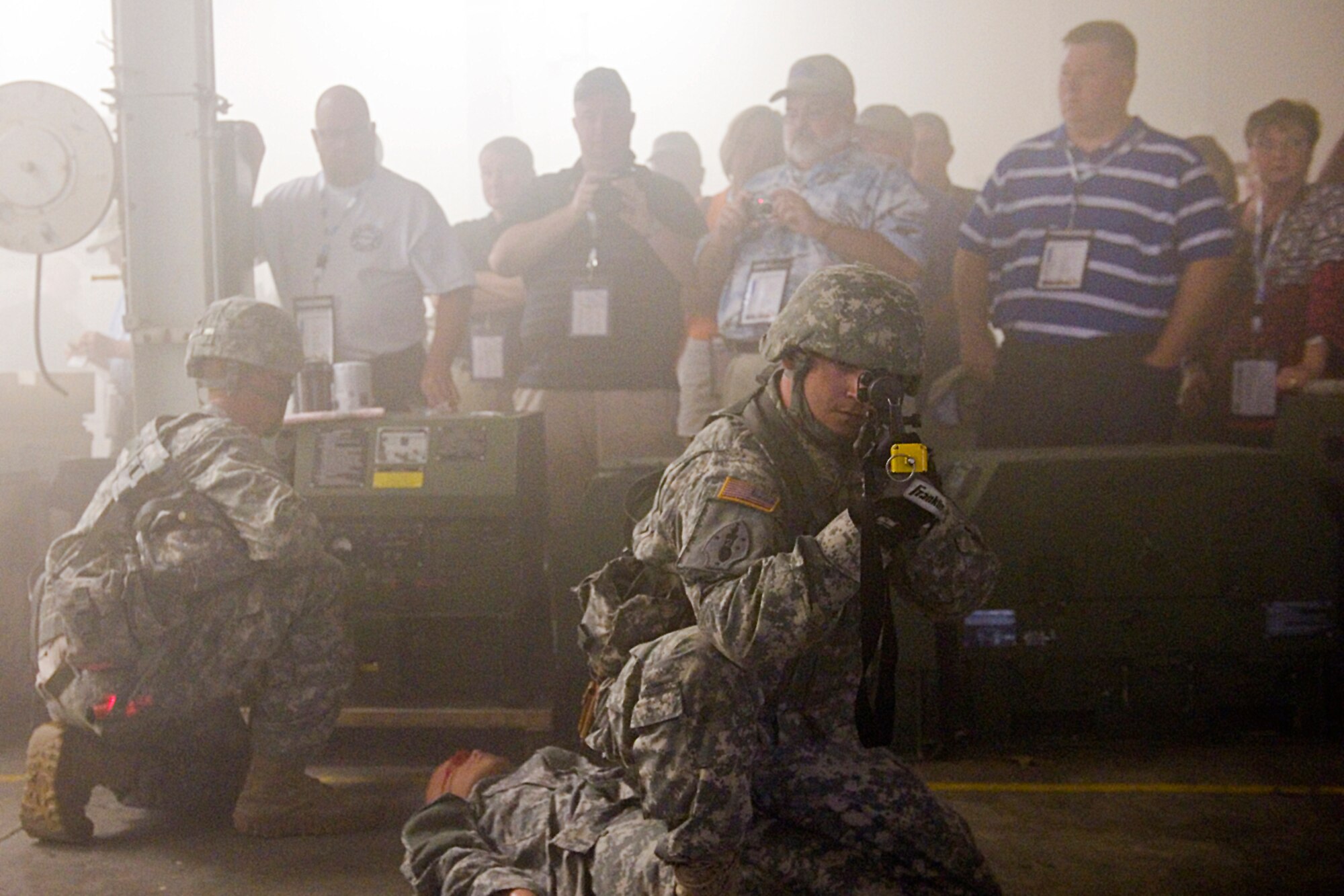 A soldier participating in a combat life saver course qualification exercise stands guard, over a mannequin in a smoke filled room, as civilians participating in an Employer Support of the Guard and Reserve tour watch at Grissom Air Reserve Base, Ind., Aug. 6, 2015.  The event was held to foster a stronger relationship between civilian employers and the Guard and Reserve. (U.S. Air Force photo/Tech. Sgt. Benjamin Mota)