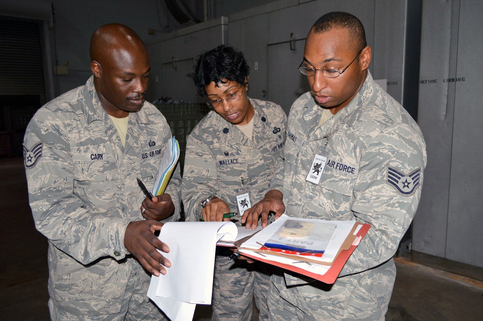 43rd Airlift Group inspection team members Staff Sgt. Derek Cary Jr., left, Lt. Col. Kimberly Wallace, center, and Staff Sgt. Roderic Thomas, right, review personnel mobility folders of Airmen processing the personnel deployment function line during an operational readiness exercise Aug. 4 at Pope Army Airfield, North Carolina. (U.S. Air Force photo/Marvin Krause)