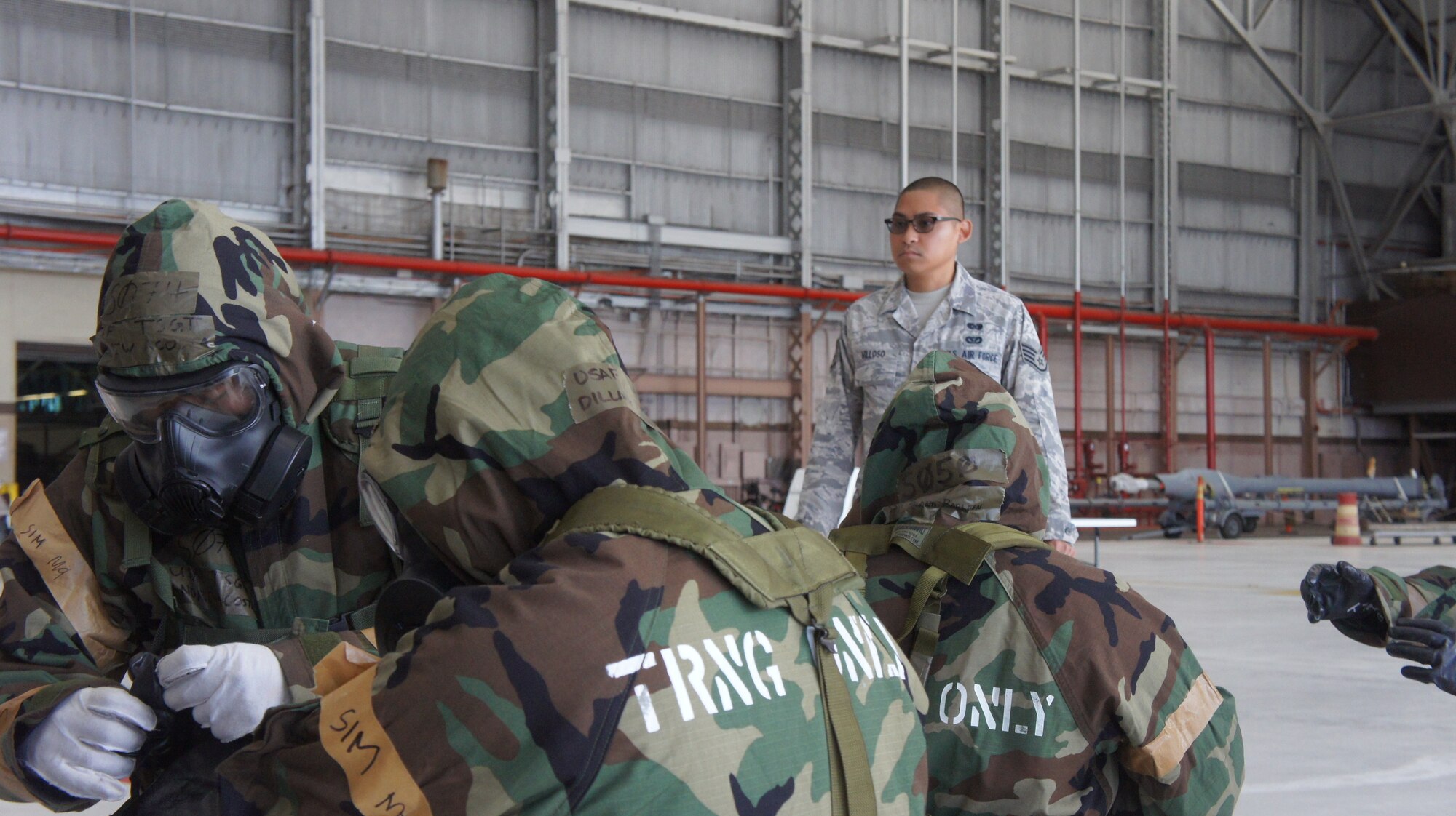 Staff Sgt. Frederick Villoso, chemical biological and nuclear environment survival instructor with the 154th Civil Engineering Squadron observes Hawaii Air National Guard Airmen as they don their chemical protective suites to MOPP 4, looking for errors and providing helpful hints, Aug. 9, 2015, Joint Base Pearl Harbor-Hickam. (U.S. Air National Guard Photo by Tech. Sgt. Andrew Jackson)