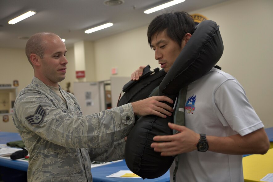 U.S. Air Force Staff Sgt. Colby Fuller, 35th Operations Support Squadron NCO in charge of aircrew flight equipment main shop, removes an emergency flotation device from an Aomori WATS basketball player at Misawa Air Base, Japan, Aug. 5, 2015. Aircrew flight equipment Airmen showed the players some of the accessories and equipment they maintain for pilots. In this instance, one of the players had the opportunity to deploy the emergency flotation device worn by pilots of the F-16 Fighting Falcon. (U.S. Air Force photo by Senior Airman Jose L. Hernandez-Domitilo)