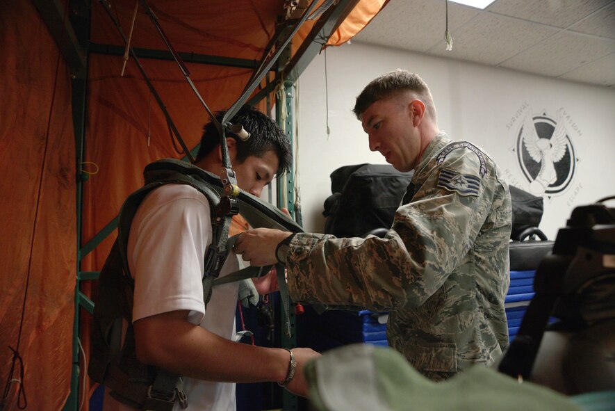 U.S. Air Force Staff Sgt. Michael Dixon, 35th Operations Support Squadron survival, evasion, resistance and escape specialist, assists an Aomori WATS basketball player in adjusting straps on a parachute landing simulator at Misawa Air Base, Japan, Aug. 5, 2015. As part of their visit to Misawa AB, the basketball players had the opportunity to learn about parachute landings and how important this training is for 35th Fighter Wing pilots. (U.S. Air Force photo by Senior Airman Jose L. Hernandez-Domitilo/Released)