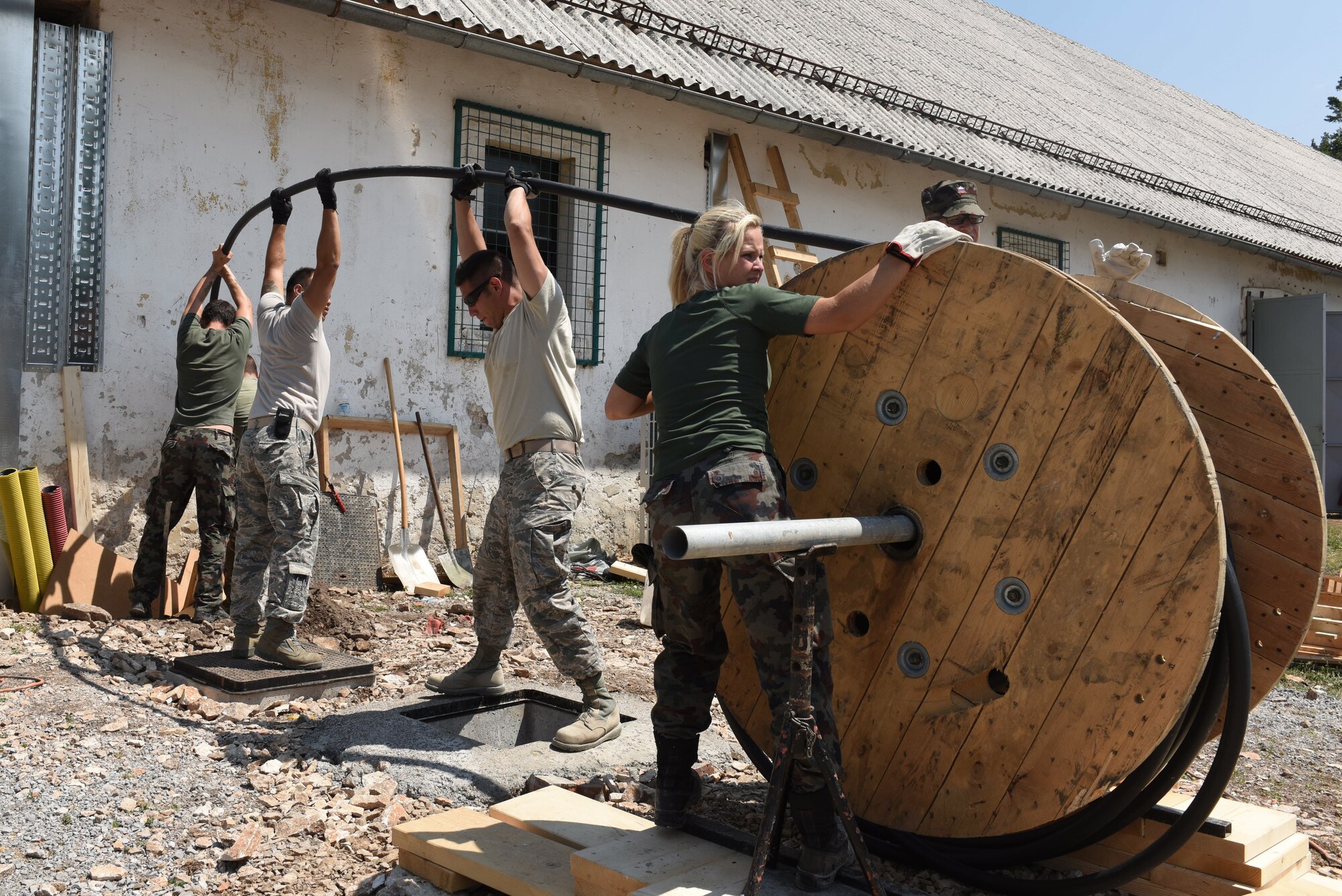 Members of the Colorado Air National Guard and  Slovenian Armed Forces (SAF) work together to pull a main power cable at Pocek Range, near Postonja, Slovenia, July 22, 2015. The SAF provided troops to assist Colorado Guardsmen restoring a historically old barn into a usable range facility to be used by SAF and NATO countries for joint, multinational training and exercises. (U.S. Air National Guard photo by Senior Airman Michelle Y. Alvarez-Rea/Released.)