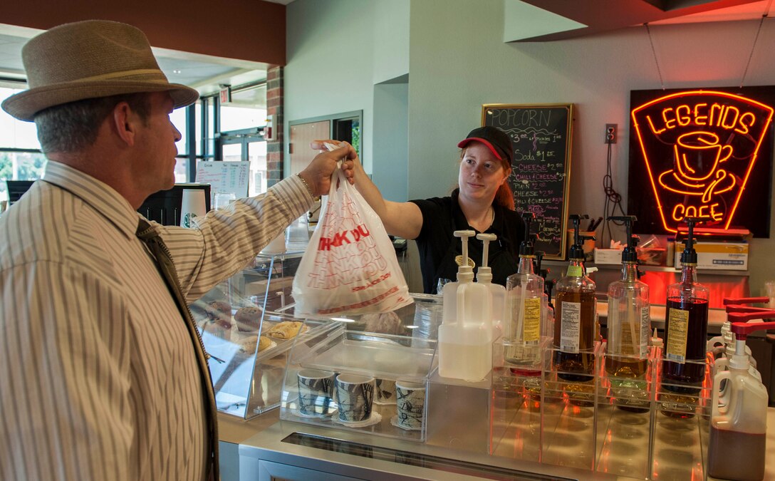 Joanna Navarro, food service worker, hands Ernest Slatinsky his lunch at the Legends Café August 5, 2015, at Dyess Air Force Base, Texas. The café is currently located in the base theater but will be moving to the Hangar Commons after updates are made to open up the building and create more space for bigger events. Legends will also be receiving a drive-thru window and an updated menu with the best items from around Abilene. (U.S. Air Force photo by Airman Quay Drawdy/Released)