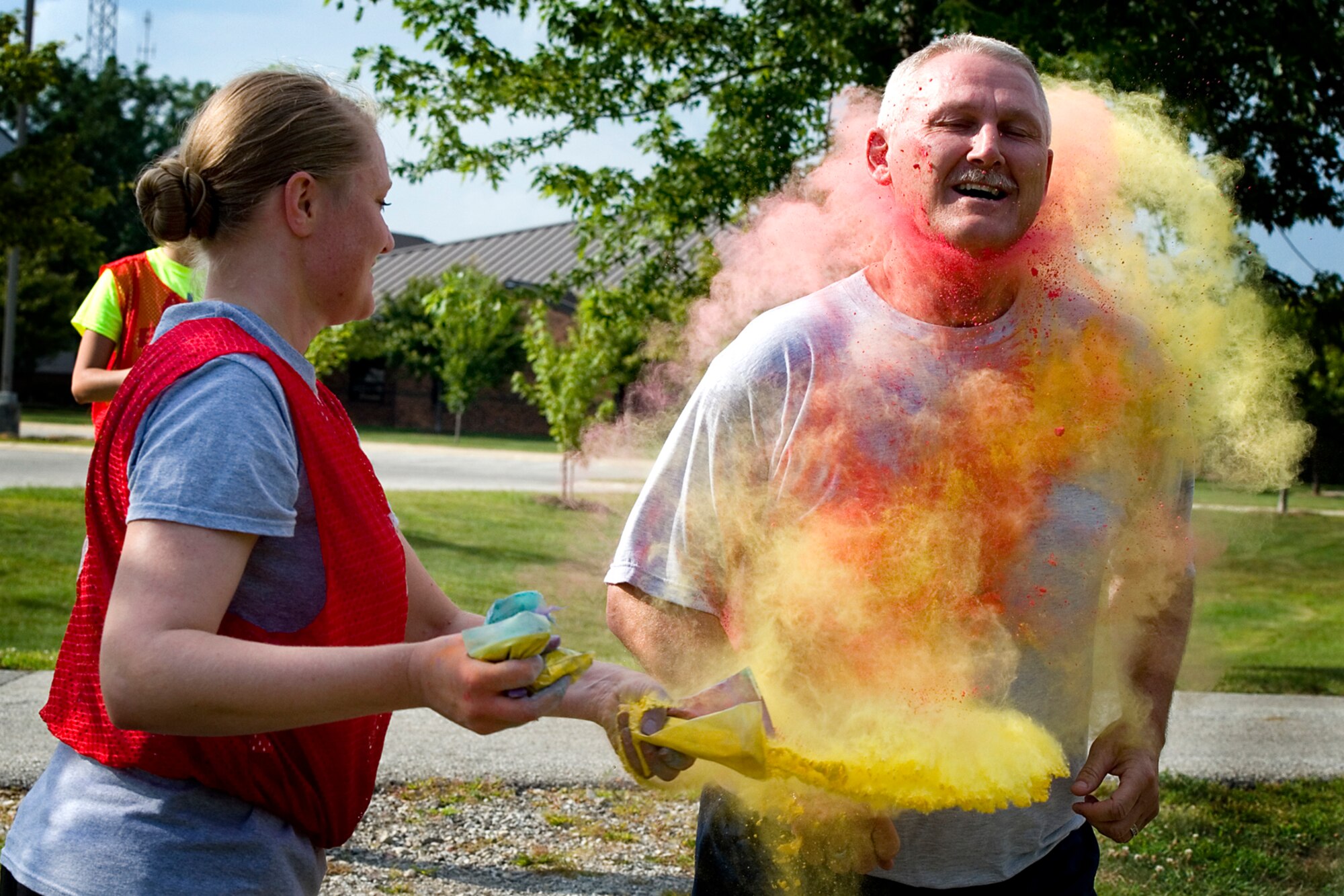 Tim Wood, base honor guard manager runs through a colorful cloud thrown at him by Christena Alotaibi, 434th Force Support Squadron support officer, during a 5k color fun run held August 8, 2015 at Grissom Air Reserve Base, Ind. Eighteen runners faced high temperatures and volunteers set on dousing them with bright colored powder. (U.S. Air Force photo/Senior Airman Jami K. Lancette)