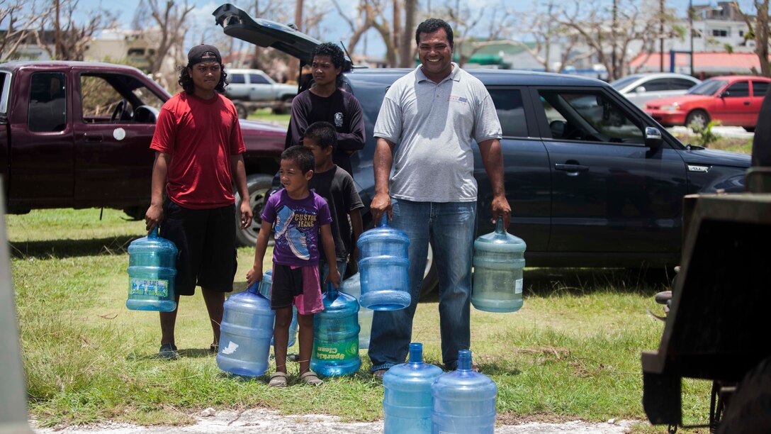 A family waits their turn for U.S. Marines with Combat Logistics Battalion 31, 31st Marine Expeditionary Unit, to fill their water jugs at a water distribution site set up as part of typhoon relief efforts in Saipan, Aug. 11, 2015. The 31st MEU and the ships of the Bonhomme Richard Amphibious Ready Group are assisting the Federal Emergency Management Agency with distributing emergency relief supplies to Saipan after the island was struck by Typhoon Soudelor Aug. 2-3.