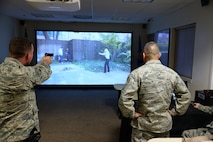 Chief Master Sgt. Gerardo Tapia, Air Education and Training Command command chief, watches as Senior Airman Cody Bower, 47th Security Forces Squadron pass and registration clerk, demonstrates a firearms simulator scenario on Laughlin Air Force Base, August 7, 2015. The Milo Range Firearms Simulator is a tool used by security forces to teach the justification of force in different scenarios. A laser is attached to the participant’s actual firearm to show where the participant’s shots land. (U.S. Air Force photo by Airman 1st Class Brandon May)(Released)