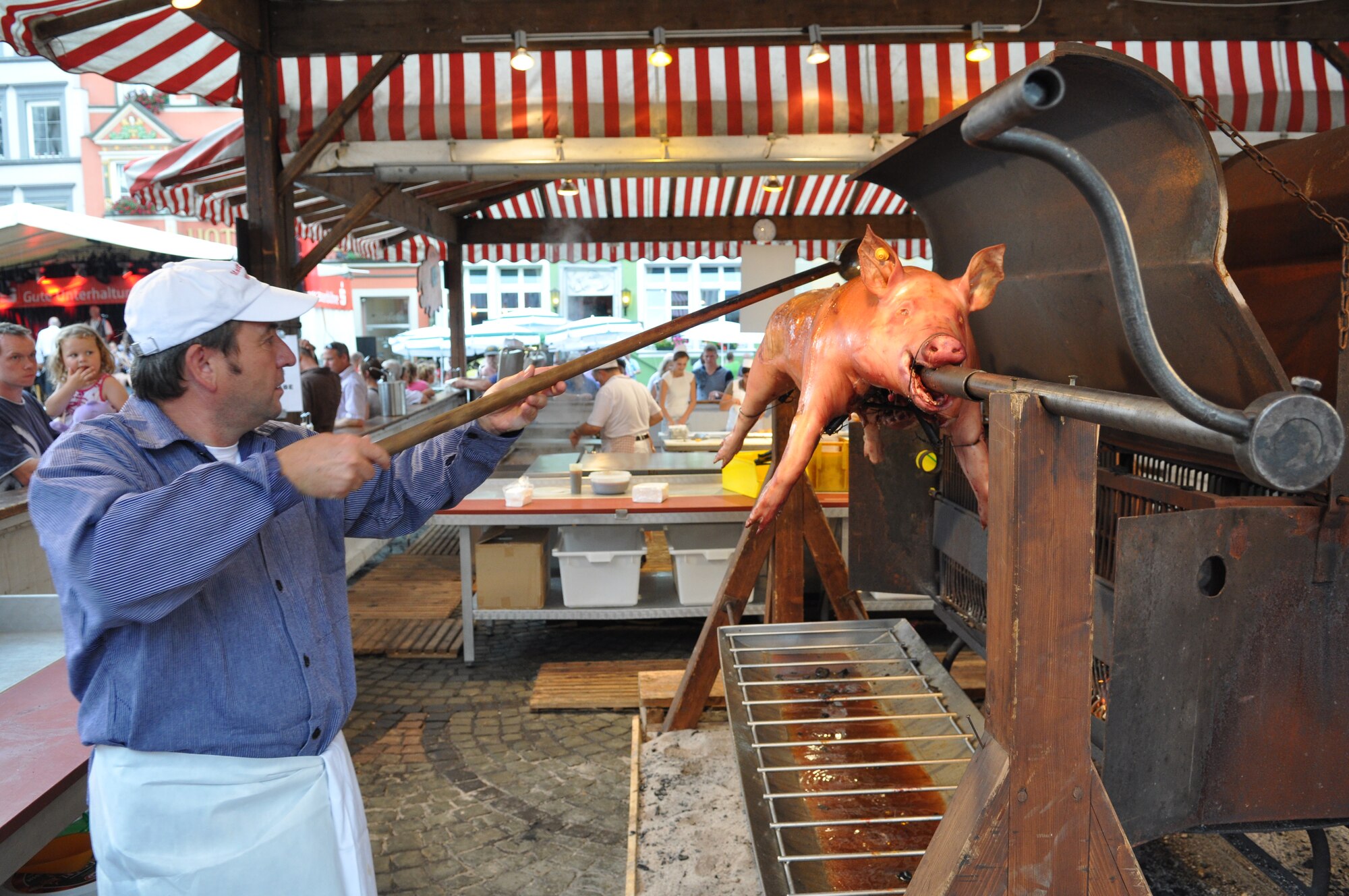 A cook prepares a roasting pig on a spit as a father with a small child watch him during the annual Pig Burner’s festival in Wittlich, Germany, Aug. 12, 2012. More than 200 pigs are sold annually at the popular "Saeubrenner Kirmes" in Wittlich, an event that attracts thousands of visitors from Germany and various other countries. (U.S. Air Force photo by Iris Reiff/Released)