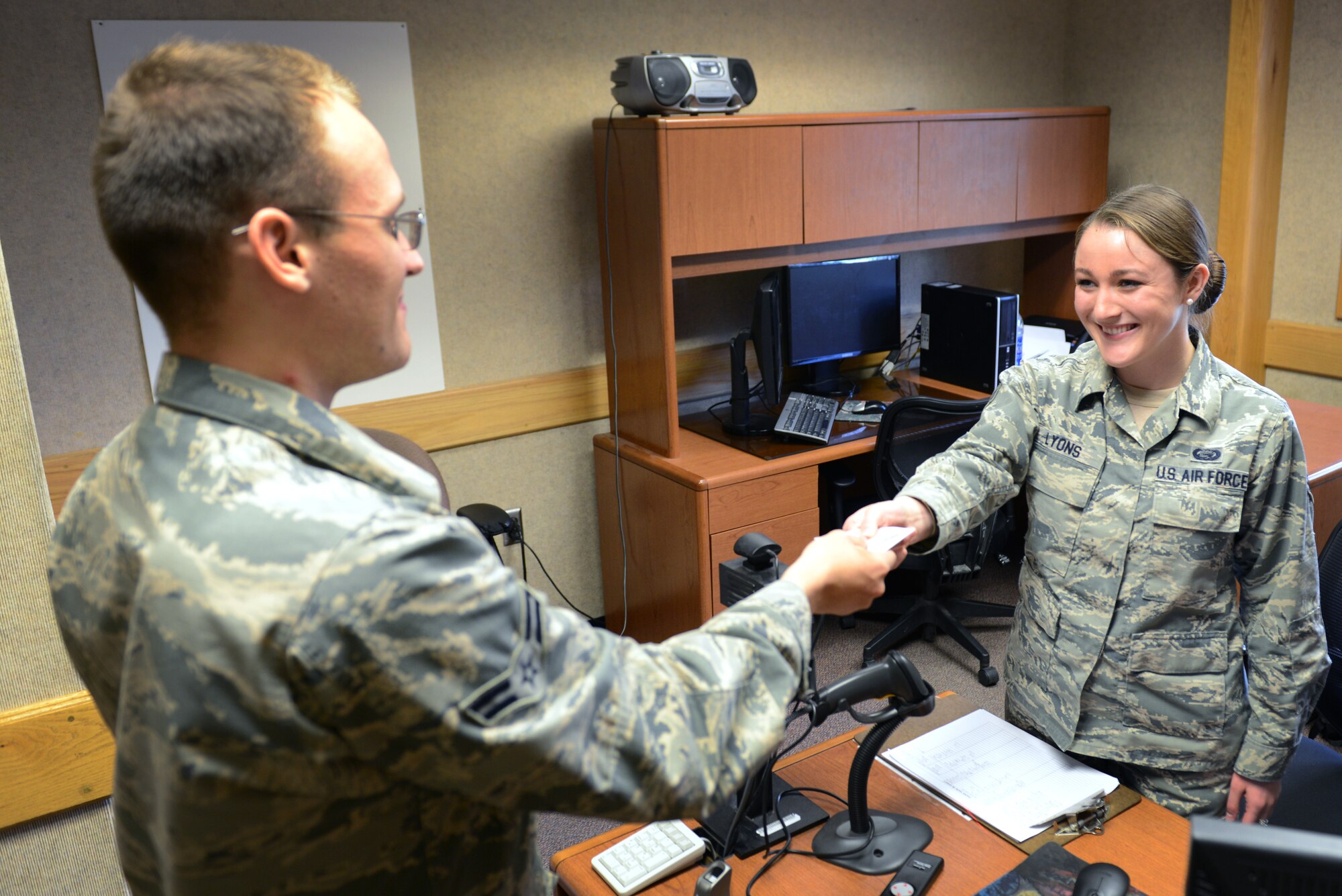 U.S. Air Force Senior Airman Alicia Lyons, a 354th Force Support Squadron career development journeyman, hands a customer his military common access card, Aug. 11, 2015, at Eielson Air Force Base, Alaska. Lyons is trained on multiple personnel sections throughout her squadron. (U.S. Air Force photo by Senior Airman Ashley Nicole Taylor/Released) 