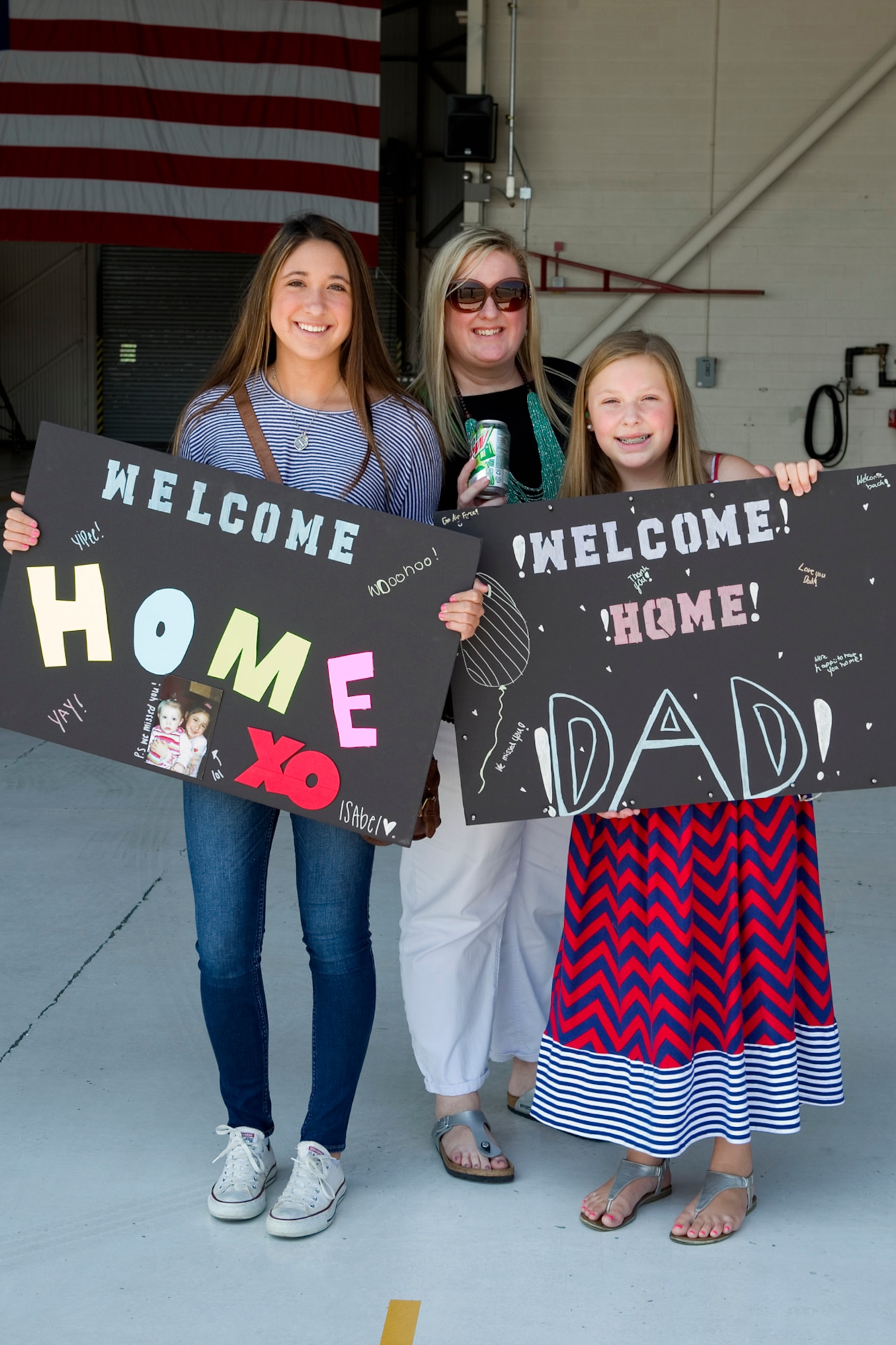 Isabel Lewis, wife of Staff Sgt. Chris Fancher, 434th Security Forces Squadron fire team leader, and his children Abbey, left, and Shelly, hold signs to greet returning Airmen at Grissom Air Reserve Base, Ind., August 8, 2015. Families and friends gathered to welcome 14 defenders home from a 180-day deployment to Southwest Asia. (U.S. Air Force photo/Tech. Sgt. Benjamin Mota)