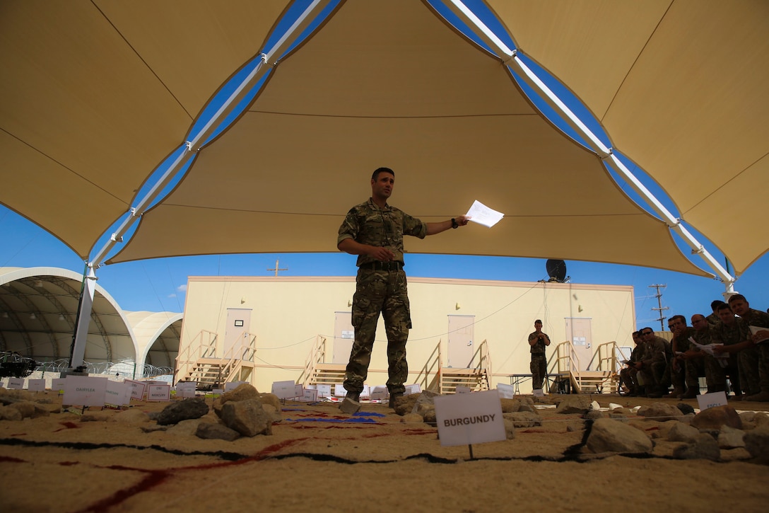 A British soldier with 2nd Marine Expeditionary Brigade explains to a crowd of U.S. Marines, Canadian and British soldiers what they are seeing on the British terrain model at a rehearsal of concept drill at Camp Wilson aboard Marine Corps Air Ground Combat Center, Calif., in support of the 2nd MEB Large Scale Exercise Aug. 12, 2015. LSE is a combined U.S. Marine Corps, Canadian, and British exercise conducted at the Brigade-level, designed to enable live, virtual and constructive training for participating forces.