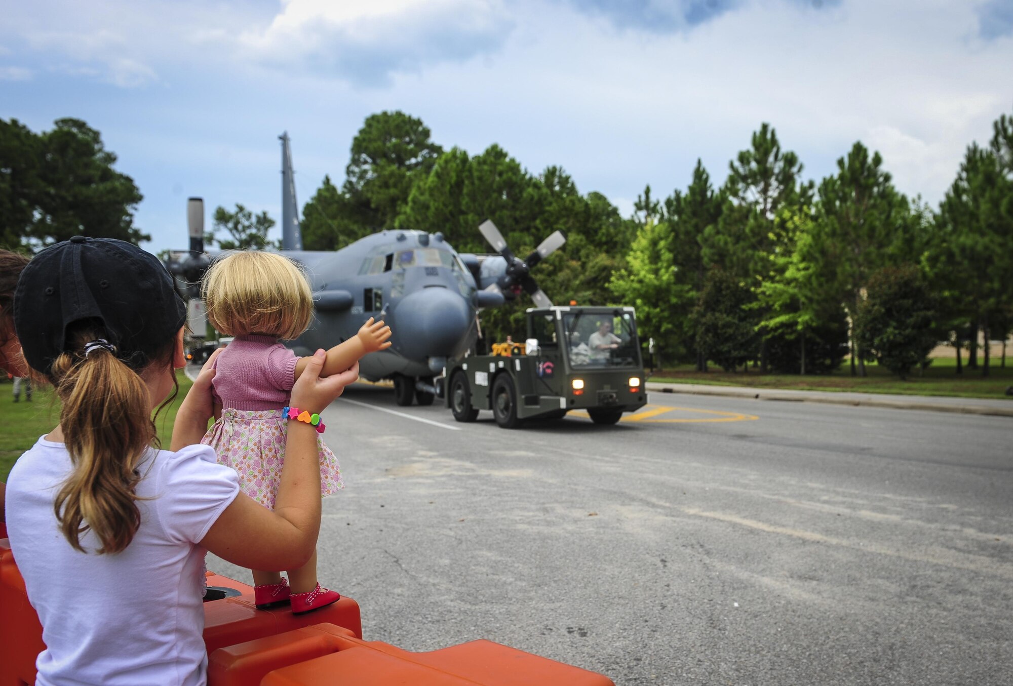 A child waves her doll’s hand as Airmen with the 1st Special Operations Aircraft Maintenance Squadron tows an AC-130H Spectre down Independence Road on Hurlburt Field, Fla., Aug. 15, 2015. The Spectre was towed from the flightline and staged for installation in to the Hurlburt Field Air Park. The AC-130H fleet retired May 26, 2015, after more than 45 years of service. The installation process for this aircraft, known as “Wicked Wanda,” is set to be complete by Aug. 28, 2015. (U.S. Air Force photo by Senior Airman Meagan Schutter/Released)