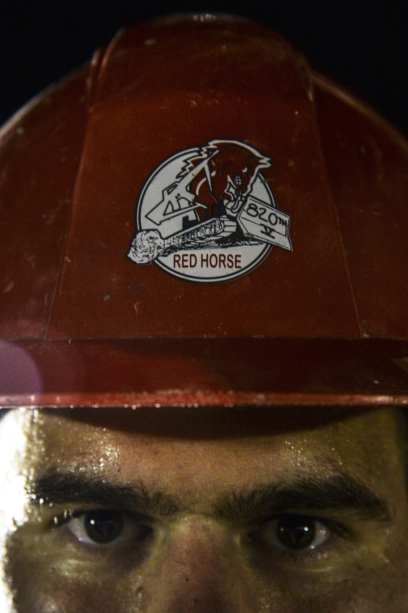 An Airman assigned to the 557th Expeditionary RED HORSE Squadron dons a red hard hat, a unique trademark of the RED HORSE community. RED HORSE, an acronym for rapid engineer deployable heavy operational repair squadron engineer, is the Air Force’s combat construction team. (U.S. Air Force photo/Tech. Sgt. Christopher Boitz)