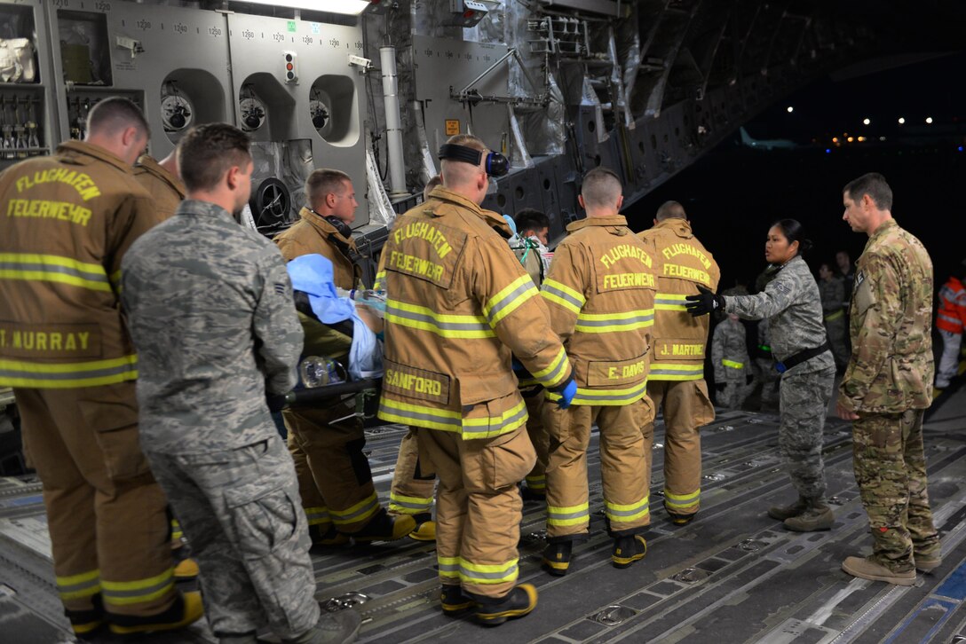 Personnel from the 86th Civil Engineer Squadron, Kaiserslautern Military Community Fire Emergency Services and 10th Aeromedical Evacuation Operations Team support 455th Expeditionary Aeromedical Evacuation Squadron Airmen with moving an injured Service member from a C-17 Globemaster III aircraft on the flight line at Ramstein Air Base Airfield, Germany, Aug. 9, 2015.  The 455th EAES Airmen are charged with the responsibility of evacuating the sick and wounded from Central Command to higher echelons of medical care. (U.S. Air Force photo by Maj. Tony Wickman/Released) 