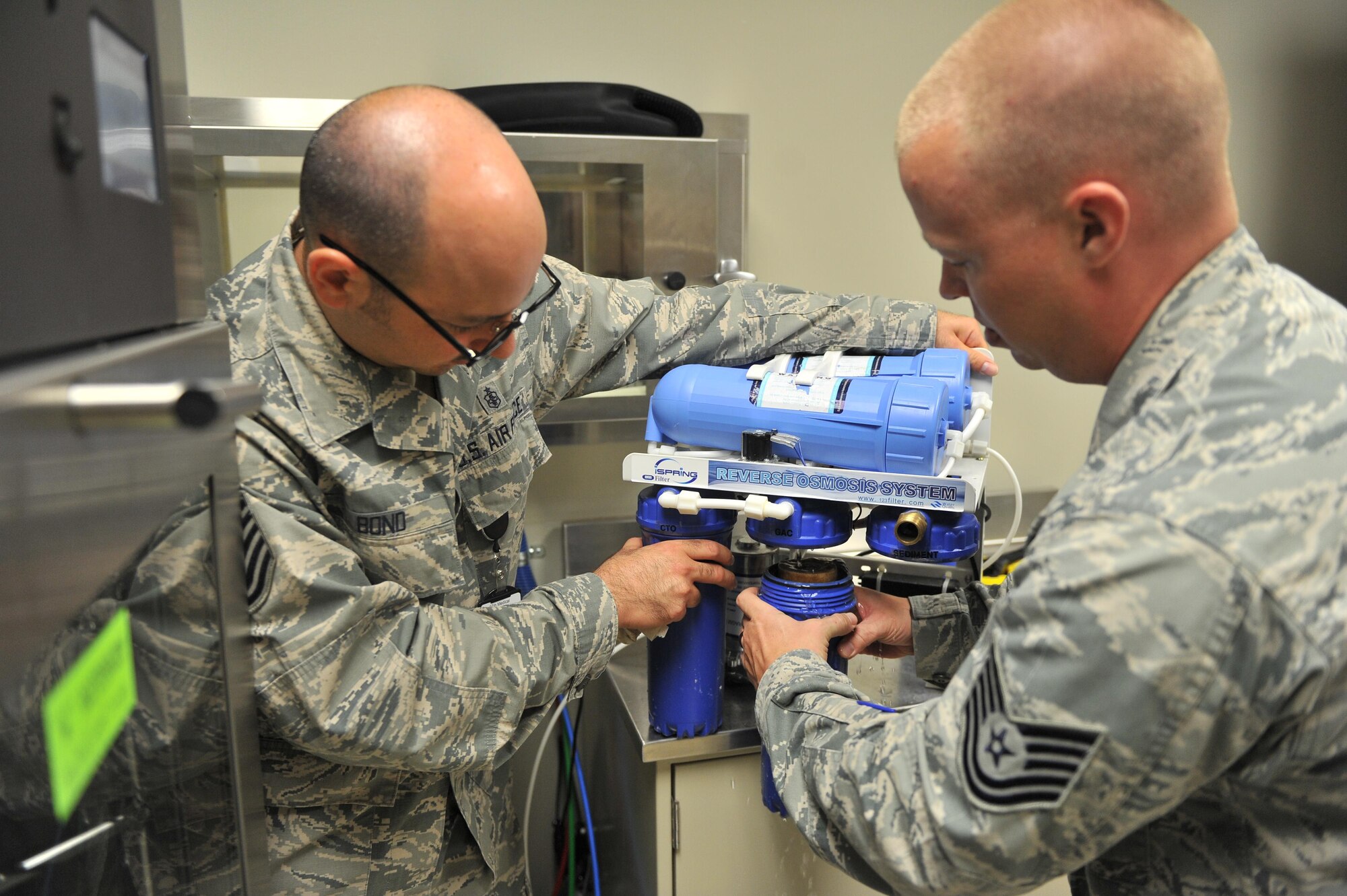 U.S. Air Force Tech. Sgts. Christian Bond and Zach Brown, 97th Medical Group bioenvironmental medical equipment technicians, change a filter on a reverse-osmosis water treatment setup inside the dental clinic at Altus Air Force Base, Oklahoma, Aug. 13, 2015. Bond and Brown change the filters monthly to ensure the dental clinic has clean water for cleaning and sanitizing dental equipment. (U.S. Air Force photo by Senior Airman Dillon Davis)