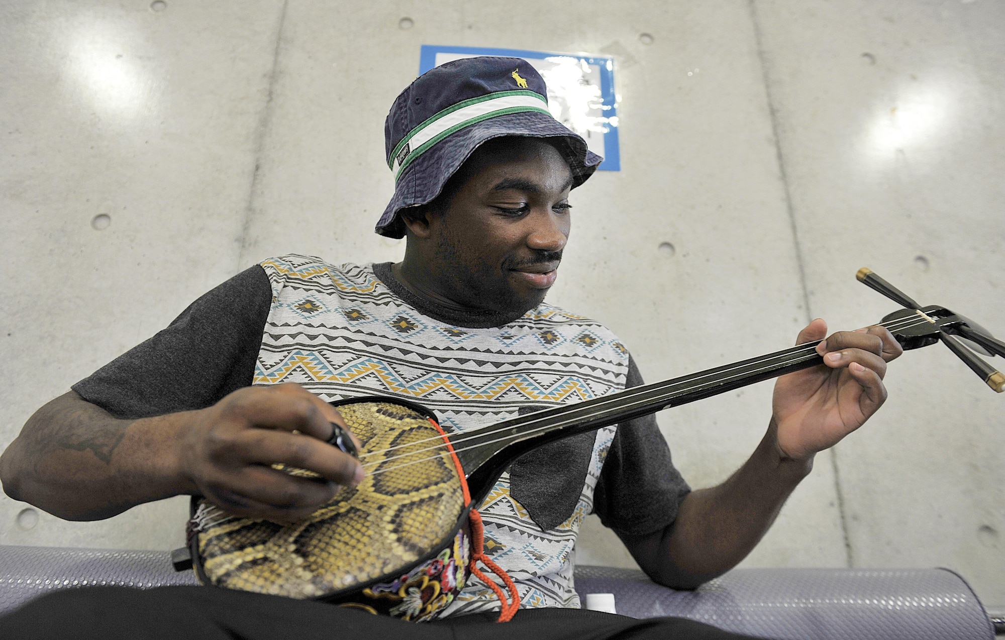 U.S. Air Force Senior Airman Kevin Inniss, 18th Communications Squadron knowledge manager, plays a Sanshin (Okinawa traditional guitar) during a culture exchange program at Kadena Rotary Plaza, Japan, Aug. 14, 2015. During the program, U.S. Air Force volunteers from the 18th Wing and Kadena Language Institute students exchanged their culture and language to improve ties between the U.S. Air Force and local community on Okinawa. (U.S. Air Force photo by Naoto Anazawa/Released)