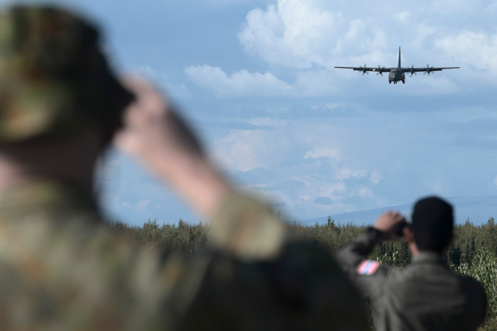 Aircrew view a C-130 Hercules low-level approach during RED FLAG-Alaska at Joint Base Elmendorf-Richardson, Alaska, Aug. 14, 2015. The training allowed C-130 aircrew to practice austere landings and take offs, combat offloads and supply drops, but also allowed friendly competition between participating Air Forces: U.S. Air Force, Japan Air Self-Defense Force, Royal Air Force, Royal Australian Air Force, Royal New Zealand Air Force and Royal Thai Air Force. Seasoned C-130 aircrew from each country judged the training exercises from the ground, allotting points based off predetermined timing and accuracy requirements. (U.S. Air Force photo by Staff Sgt. Cody H. Ramirez/Released)