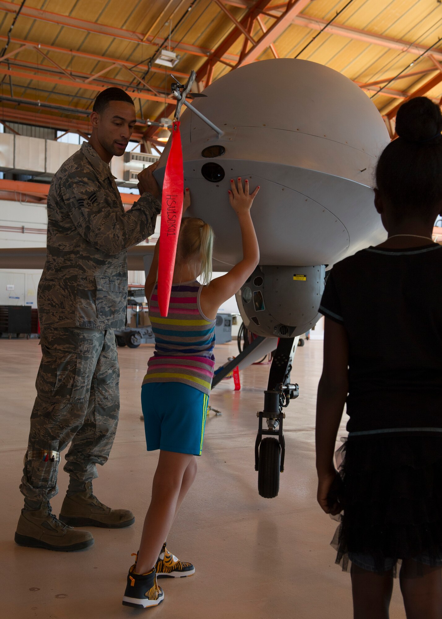 Senior Airman Elijah Rogers, a 49th Aircraft Maintenance Squadron MQ-1 Predator avionic systems journeyman, shows members from the Holloman Youth Center how light the MQ-1 is by lifting the front end off the ground at Holloman Air Force Base, N.M. on Aug. 12. Children from the youth center visited the 49th AMXS and spoke with maintainers about the capabilities of Holloman’s Remotely Piloted Aircraft. The tour was also part of the Tuskegee Airmen Initiative that supports children’s interest and knowledge in fields of aviation. (U.S. Air Force photo by Senior Airman Leah Ferrante)