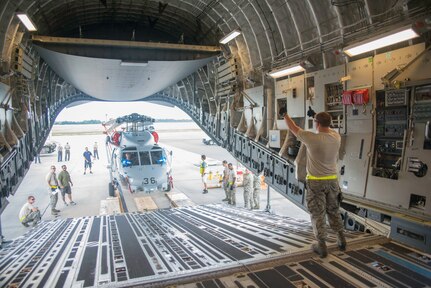 Senior Airman Garrett Hampton, 437 Aerial Port Squadron freight loading supervisor, guides a team of Airmen and representatives from General Dynamics and Sikorsky Aircraft as they load the final shipment of  Seahawk S-70B (SH-16 in Brazilian service) onto a C-17 Aug. 8. The shipment, included two SH16s and associated parts and was worth more than $100 million. These helicopters were the last of six being shipped as part of the modernization of the Brazilian helicopter fleet. A team of several Brazilian helicopter pilots who were in Maryland receiving training on how to operate their newest aircraft traveled to Charleston to oversee the shipment. Doing so allowed them to meet with the team that made this delivery possible. “I really enjoy loading things like that,” said Hampton. “We rarely get to see who it is we are loading cargo for, so opportunities like that are fun.” (U.S. Air Force photo/Staff Sgt. William A. O’Brien)