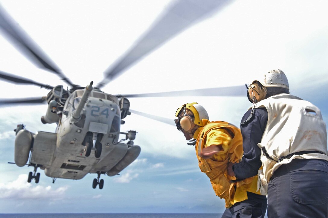 U.S. Navy Petty Officer 1st Class Myisha Buckhalder holds Seaman Richard Porter as a CH-53E Super Stallion takes off from the flight deck of the amphibious dock landing ship USS Ashland after offloading weapons in the Pacific Ocean, Aug. 17, 2015. The Ashland is patrolling in the U.S. 7th Fleet area of operations. U.S. Navy photo by Petty Officer 3rd Class David A. Cox
