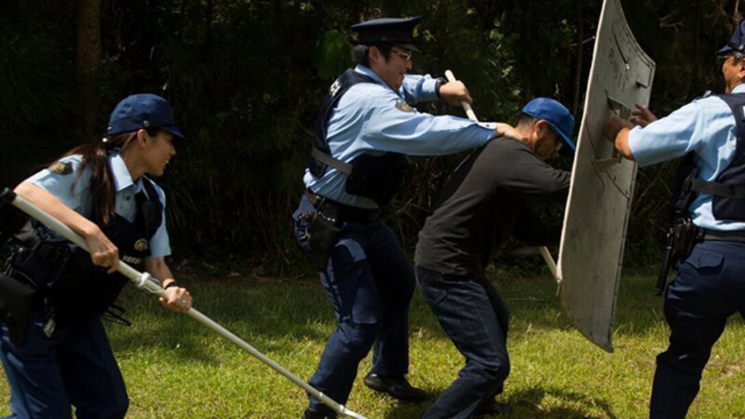 Ishikawa police officers Chikae Higa, left, Satoshi Goto, center, and Hisakazu Higa detain a simulated aggressive trespasser, Takao Agarijo, during a bilateral scenario-based training exercise on Camp Hansen, Okinawa, Japan, Aug. 5, 2015. The training increased teamwork between Ishikawa Police Station and the Marine Corps Base Camp Smedley D. Butler Provost Marshal's Office, Precinct North, Camp Hansen. 