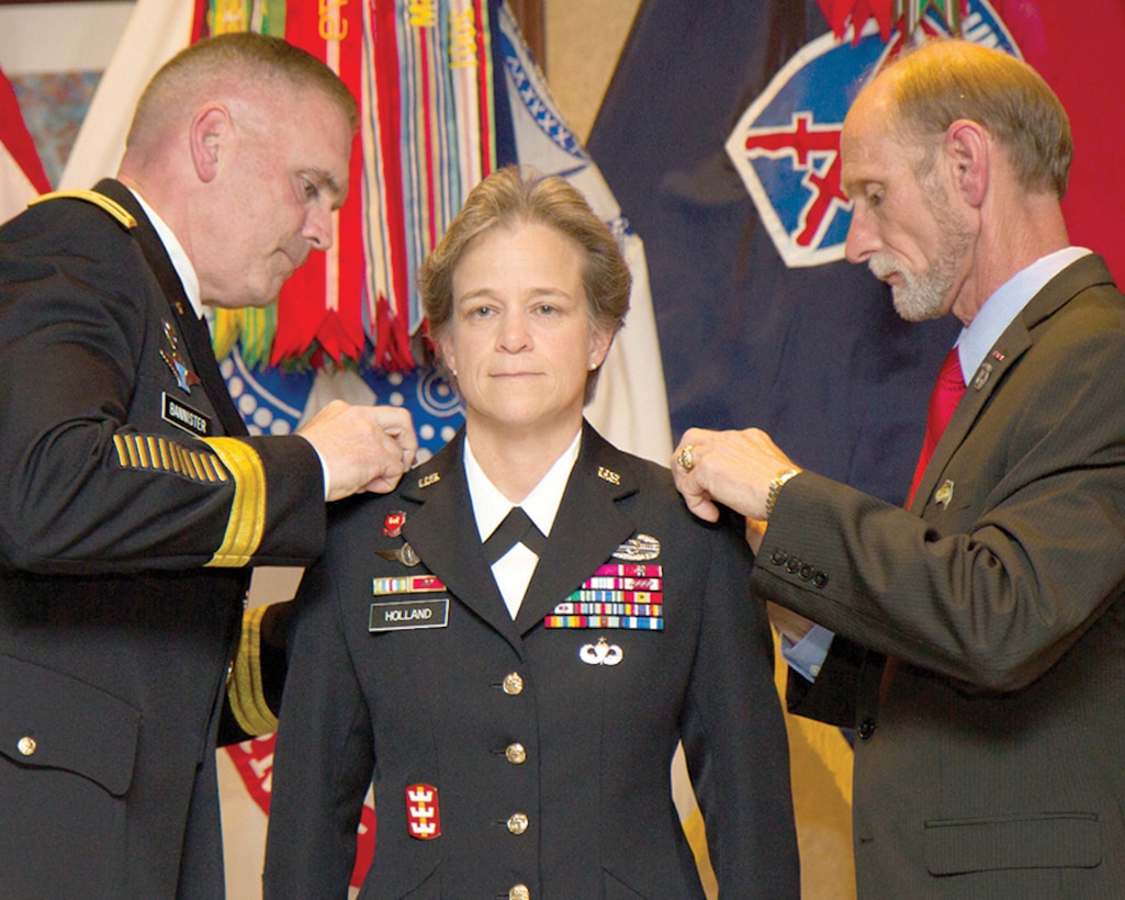 Army Col. Diana Holland, 10th Mountain Division deputy commander for support, becomes the first woman to hold the title of deputy commanding general for support in a light infantry division during her promotion ceremony to brigadier general on Fort Drum, N.Y., July 29, 2015. Her husband, James Holland Jr., right, and Army Maj. Gen. Jeffrey L. Bannister, 10th Mountain Division and Fort Drum commander, pin on her new stars. U.S. Army photo by Spc. Osama Ayyad