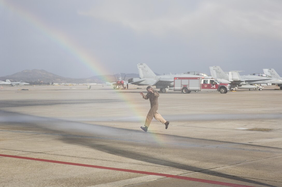 Col. John Farnam, commanding officer of Marine Corps Air Station Miramar, runs through an artificial shower after conducting his last flight as commanding officer aboard MCAS Miramar, California, August 17. Marines and family members celebrated his last flight as MCAS Miramar’s commanding officer with a traditional “wet down.” (U.S. Marine Corps photo by Sgt. Lillian Stephens/Released)