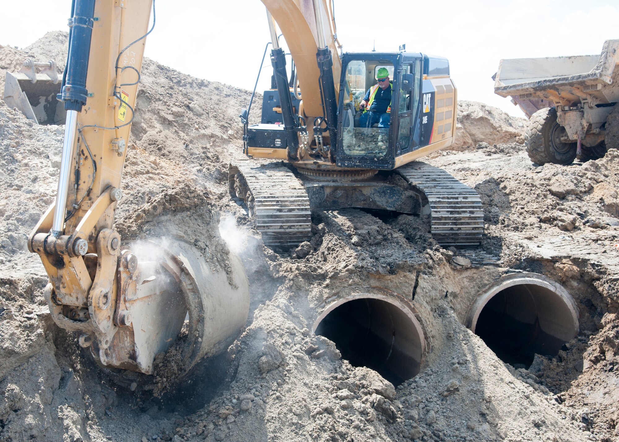 An excavator removes concrete piping August 12, 2015, on Dover Air Force Base, Del. during Dover AFB’s $98.3M runway repair project.  The old culvert material consists of hundreds of feet of reinforced concrete piping which is being replaced with a stronger, larger concrete box design. (U.S. Air Force photo/Senior Airman Jared Duhon)