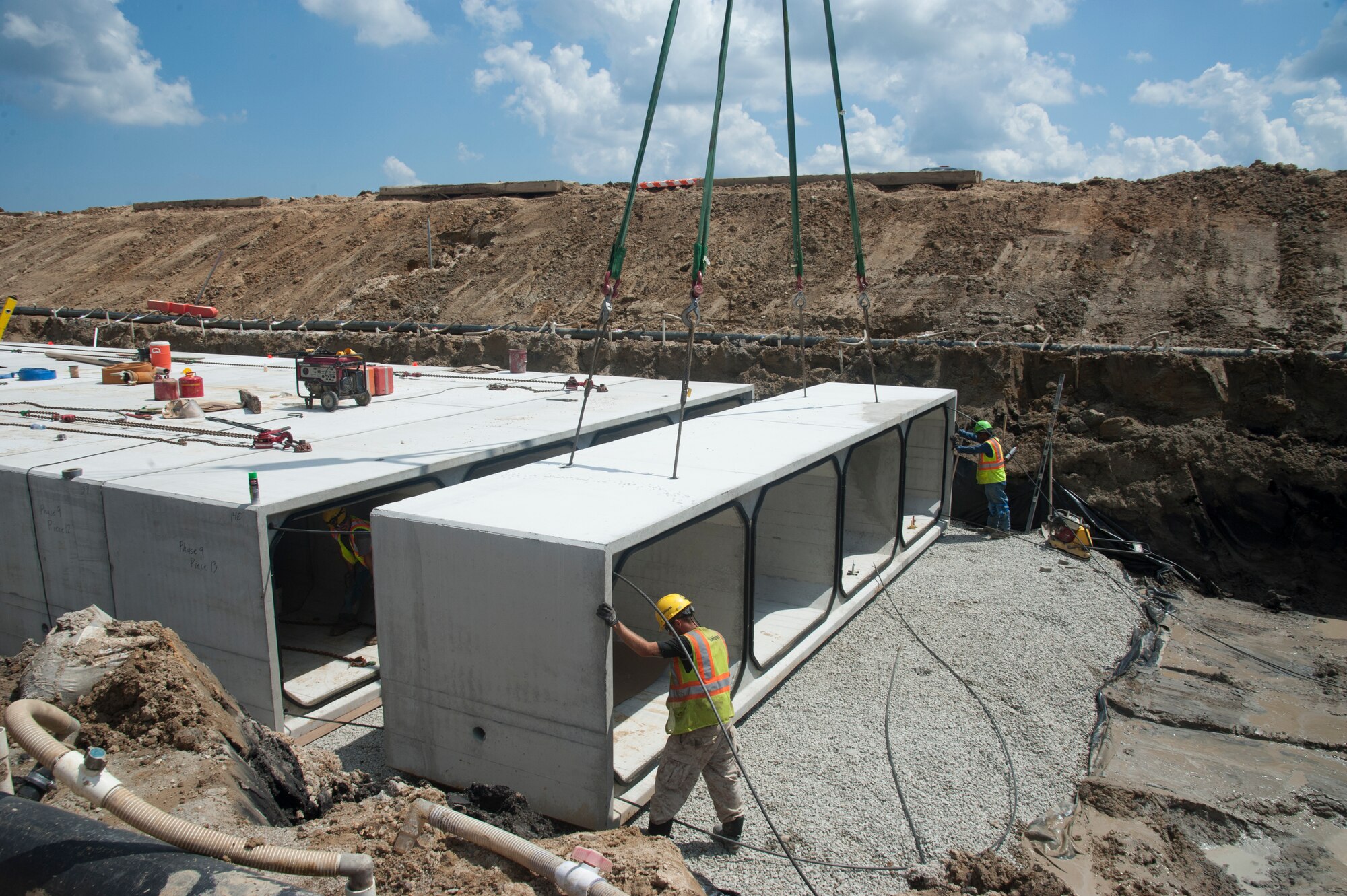 Construction workers finesse a concrete box into position August 12, 2015 on Dover Air Force Base, Del. during Dover AFB’s $98.3M runway repair project.  Each section of the culvert is placed, cinched, tarred, covered with dirt and compacted to ensure storm water does not leak and is effectively drained off the airfield. (U.S. Air Force photo/Senior Airman Jared Duhon)