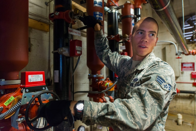 Senior Airman Dominic Koah, 11th Civil Engineer Squadron water and fuels systems specialist, discusses the proper maintenance procedures with his crew member at Hangar 13 on Joint Base Andrews, Md., Aug. 19, 2015. Before maintenance could begin, the team had to ensure all the fire suppression system components were turned off. (U.S. Air Force photo by Staff Sgt. Chad C. Strohmeyer)(Released)