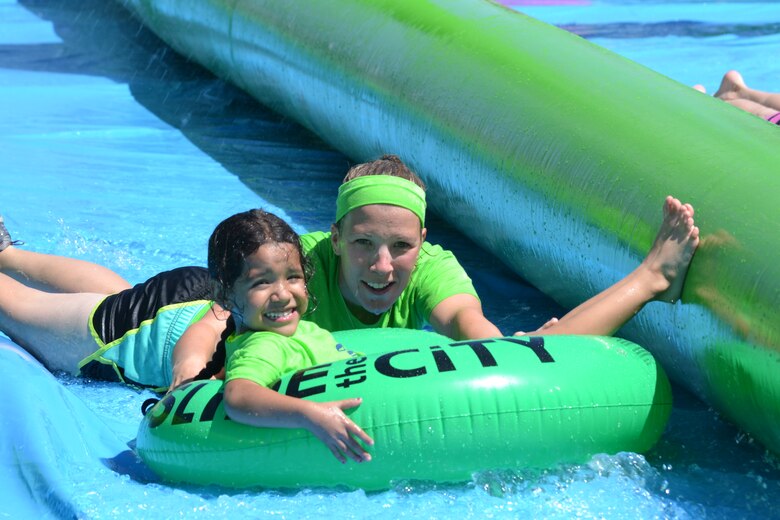 Kristin Moseley, Schriever School Age Program assistant, helps push Adrienne Sanchez, SAP student, down the giant slip-and-slide during Operation Slide Schriever Friday, Aug. 14, 2015, at Schriever Air Force Base, Colorado. Hundreds of people turned out for the free event which also included food, drinks and a kid’s zone. (U.S. Air Force photo/Brian Hagberg)