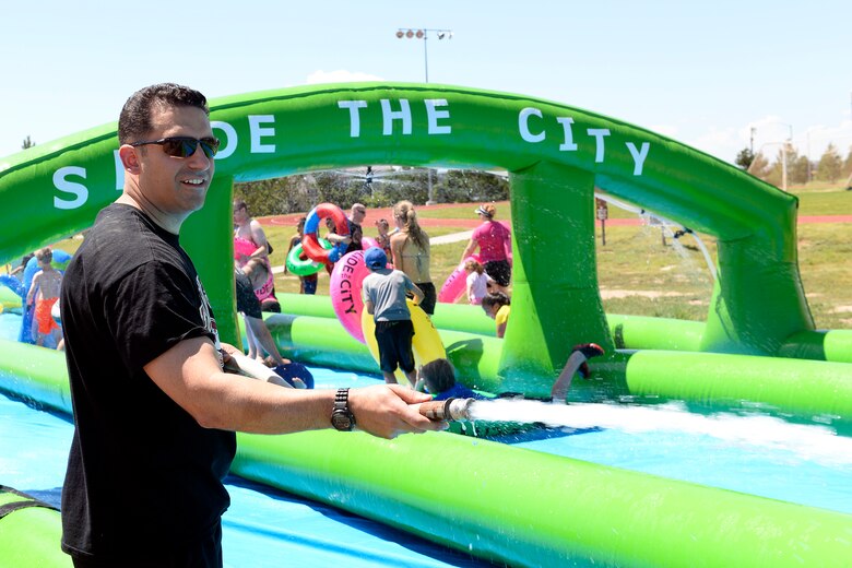 Col. Jason Janaros, 50th Mission Support Group commander, sprays water on participants sliding down the giant slip-and-slide during Operation Slide Schriever Friday, Aug. 14, 2015 at Schriever Air Force Base, Colorado. Hundreds of people turned out for the free event, including youth from the Schriever School Age Program and Ellicott School District. (U.S. Air Force photo/Christopher DeWitt)