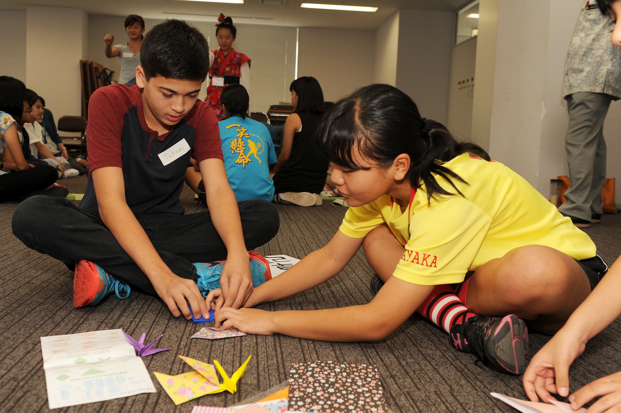Sayaka Teruya, a Kokura Junior High School student, teaches Takumi Irwin, a Kadena Middle School student, to fold an origami crane at an English Summer Camp in Naha, Japan, Aug. 14, 2015. At the camp, American middle and high school students learned about Japanese culture by playing games and speaking to Japanese elementary and middle school students, which gave the Japanese children the opportunity to practice their conversational English skills. (U.S. Air Force photo by Airman 1st Class Zade C. Vadnais)