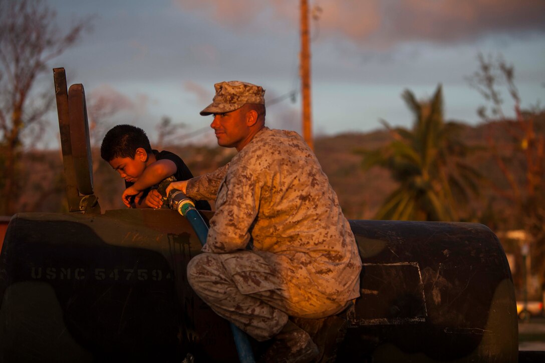 U.S. Marine Gunnery Sgt. Randy Weiss with Combat Logistics Battalion 31, 31st Marine Expeditionary Unit, lets a young boy help fill a water bull during typhoon relief efforts in Saipan, Aug. 12, 2015. The 31st MEU and the ships of the Bonhomme Richard Amphibious Ready Group are assisting local and federal agencies with distributing emergency relief supplies to Saipan after the island was struck by Typhoon Soudelor Aug. 2-3. (U.S. Marine Corps photo by Gunnery Sgt. Ismael Pena/Released)