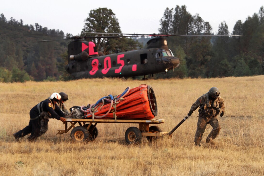 Cal Fire's Capt. Frank Abril, left, the military helicopter manager, and Army Sgts. Jameson Freymond and Matthew Hammond use a cart to move a  bucket firefighting system to hook it up to a CH-47 Chinook helicopter in Redding, Calif., Aug. 19, 2015. Freymond, a flight engineer, and Hammond, a crew chief, are assigned to the California Army National Guard's 1st Battalion, 126th Aviation Regiment. California Army National Guard photo by Staff Sgt. Eddie Siguenza
