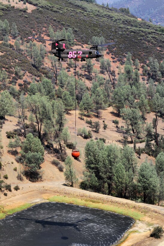 A CH-47 Chinook helicopter leaves the Alden Gulch dip site after filling up a bucket with water in Shasta County, Calif., Aug. 19, 2015, to continue fighting Northern California’s wildfires. The helicopter crew is assigned to the Nevada National Guard. California Army National Guard photo by Staff Sgt. Eddie Siguenza