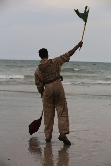 Lance Cpl. Rameses Spellman, a Crewman with 1st Platoon, Bravo Company,2nd  Assault Amphibian  Battalion waves a flag to signal the go ahead for the next amphibious assault vehicle to start their push into the surf on Onslow Beach aboard Camp Lejeune, N.C. Aug. 17, 2015. During this training exercise the battalion conducted gator squares and beach assaults. (U.S. Marine Corps photo by Pfc. Miranda Faughn/Released)