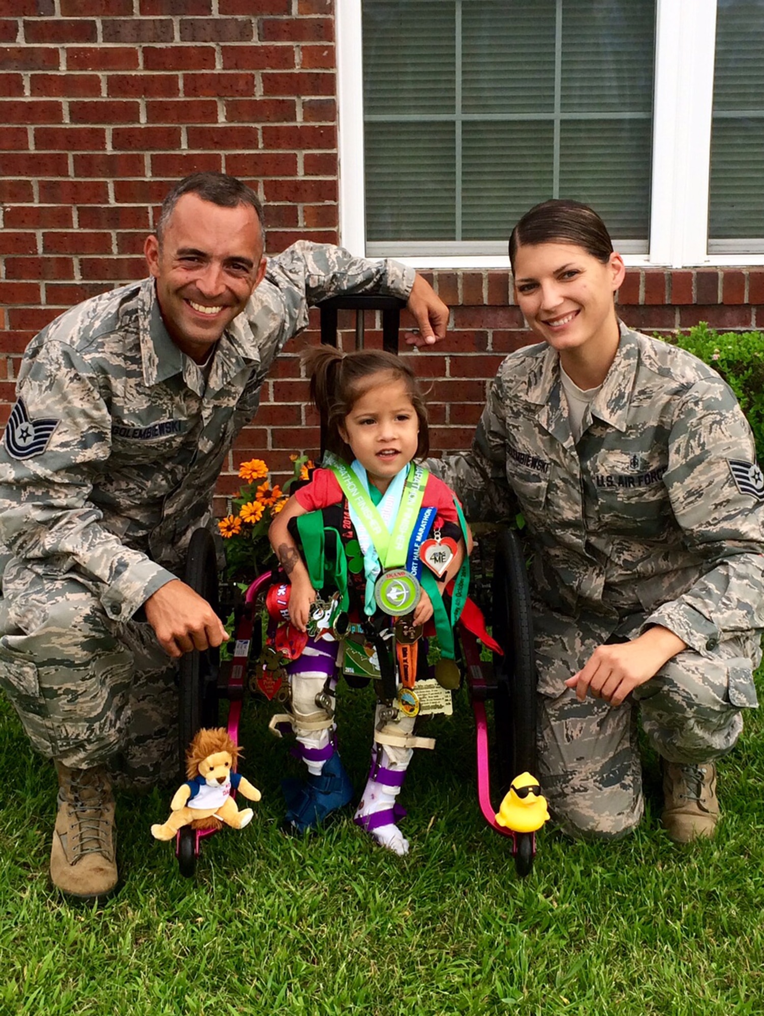 Tech. Sgt. Paul Golembiewski and Tech. Sgt. Amanda Golembiewski flank their daughter Grace, who is wearing medals earned by Helen Hart, a British woman from Derbyshire, England, who plans to run the U.S. Air Force Marathon (Half) Sept. 19. Hart runs in honor of Grace, who was born with arthrogryposis multiplex congenita at birth, and sends the 2-year-old all her medals and racing bibs. (Contributed photo)