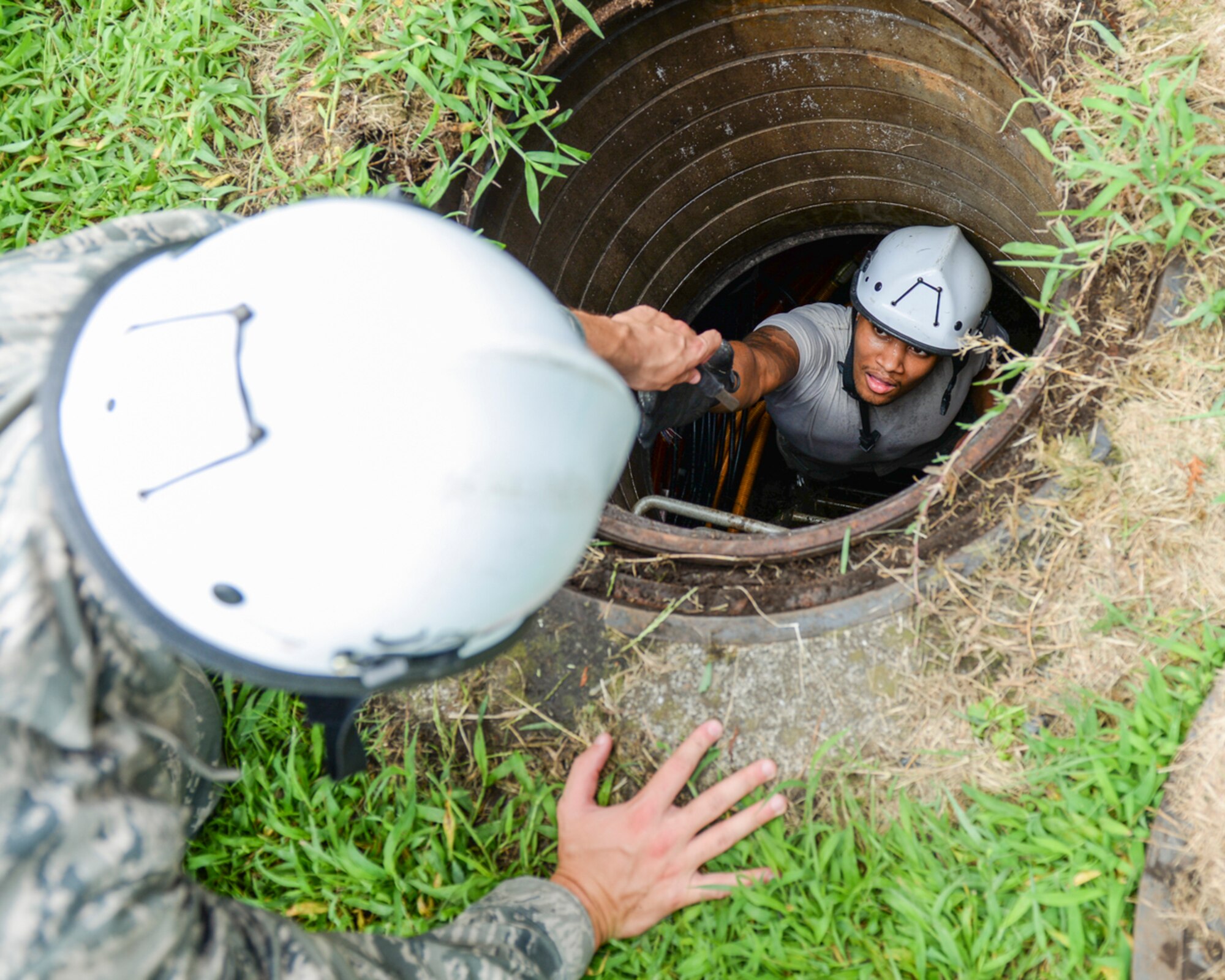 An Airman hands a tool to Senior Airmen Chris Carter, both 374th Communications Squadron cable and antenna systems technicians, at Yokota Air Base, Japan, Aug. 18, 2015. After installing newer and more efficient fiber optic cables, The 374th CS cut out 15,000 ft. of old copper cable running between the high school field and the 374th Security Forces Squadron canine building. (U.S. Air Force photo by Airman 1st Class Elizabeth Baker/Released)
