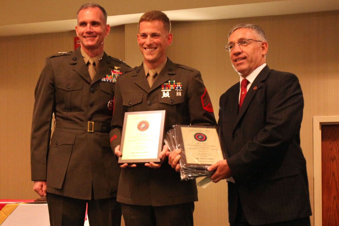Maj. Gen. Gary Thomas, left and Manny Pacheco, right, present Sgt. Reece Lodder with multiple awards during the U.S. Marine Corps Combat Correspondents Association awards banquet at the Hilton Double Tree Hotel in New Bern, North Carolina, Aug. 19, 2015. The USMCCCA hosted the banquet to honor distinguished guests and award winners in the combat correspondents community. Thomas is the commanding general of 2nd Marine Aircraft Wing. Lodder is a mass communications specialist with USMC Recruiting Station Seattle. Pacheco is the president of the USMCCCA.