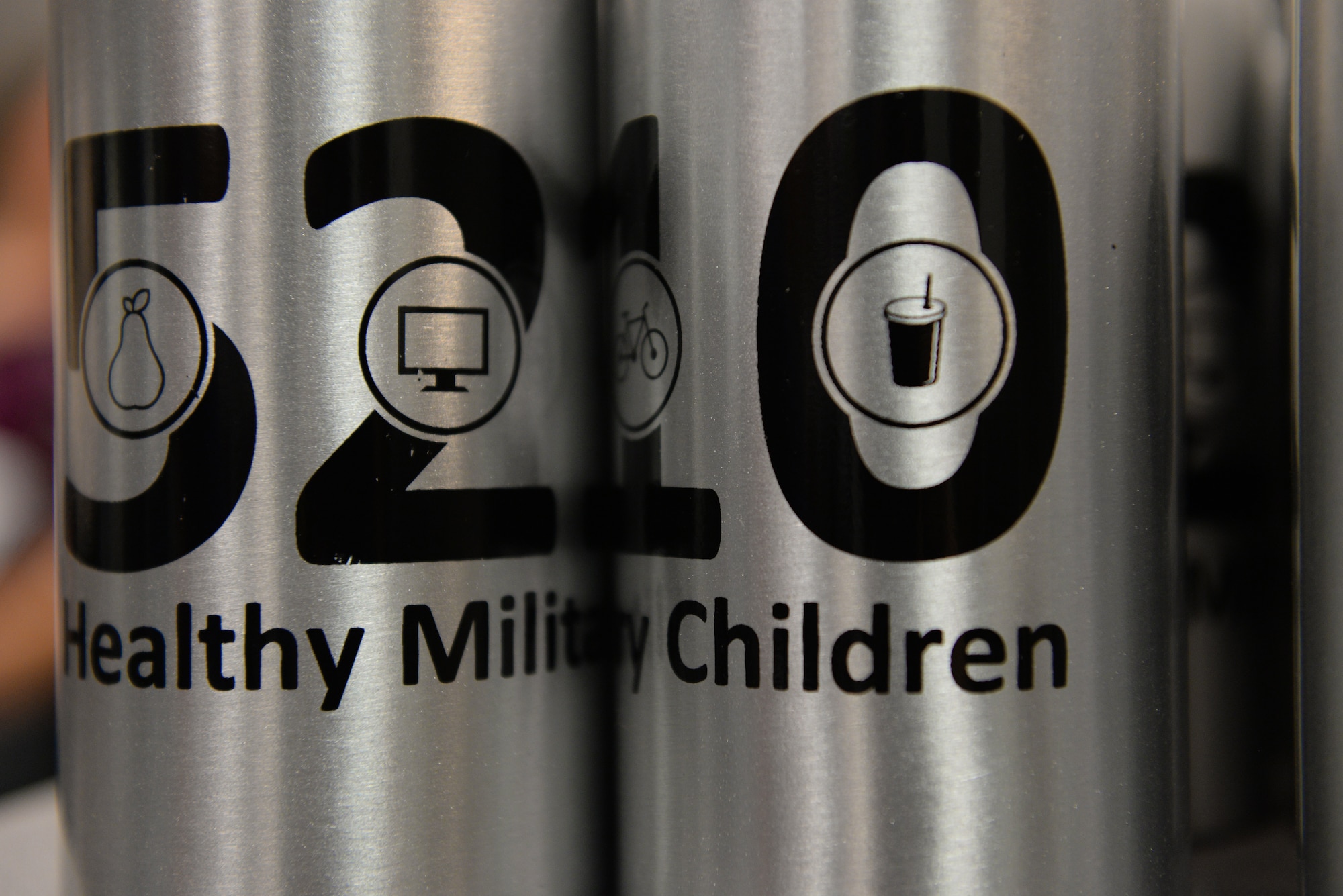 Water bottles with the 5210 Healthy Military Children program logo sit during a cooking class called ‘EMFP Garden to Table Cooking Class’, August 6, 2015 at Scott Air Force Base, Illinois. The HMC program’s goal is to reduce screen time, add one hour of activity, and eat five servings of fruits and vegetables each day. (U.S. Air Force photo by Airman 1st Class Erica Holbert-Siebert)