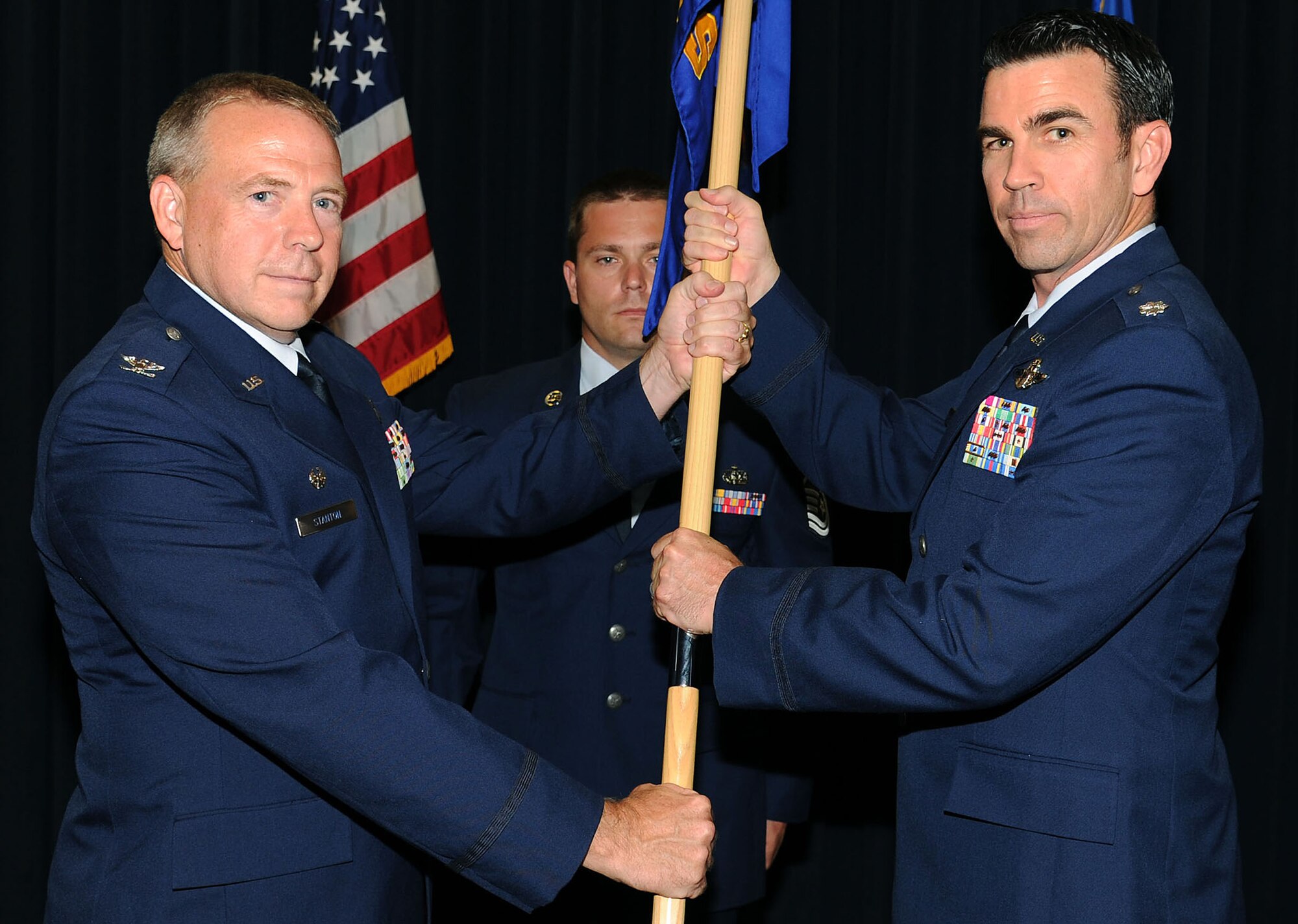 Lt. Col. Mark Richey, right, accepts the Operations Support Squadron guideon from Col. Robert Stanton, 302nd Operations Group commander during a change of command ceremony Aug. 2, 2015. Richey joined the 302nd Airlift Wing in 2012. Master Sgt. Jason Zuress, center, is the first sergeant for the 302nd OSS. (U.S. Air Force photo/Senior Airman Amber Sorsek)