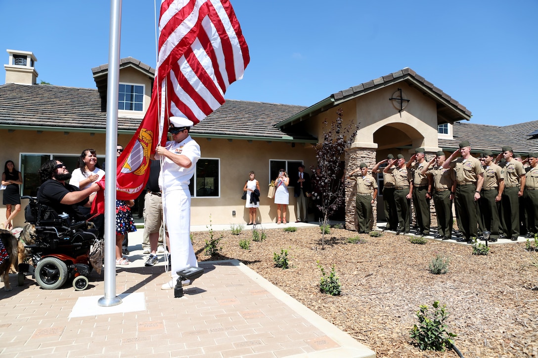 Marines from 1st Explosive Ordnance Disposal Company, 1st Marine Logistics Group look on as retired Staff Sgt. Jason Ross raises the national and Marine Corps colors in front of a new home dedicated to him and his family by The Gary Sinise Foundation in Fallbrook, California, August 21, 2015. Ross was injured by an improvised explosive device in Afghanistan in 2011 while serving as an explosive ordnance disposal technician and lost both of his legs as a result. The new home has smart technology that will significantly reduce the difficulty of everyday tasks for Ross and allow him and his family to live more comfortably.